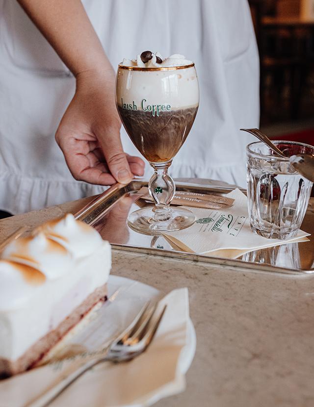 Kellnerin serviert Irish Coffee im Glas und hausgemachte Baiser-Torte im Café Tomaselli