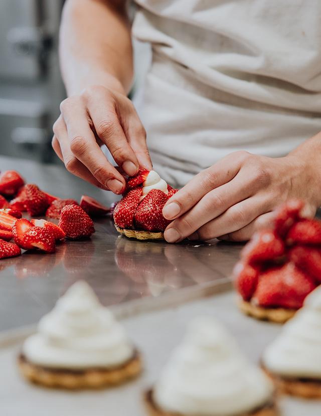 Unser Zuckerbäcker belegt süße Törtchen mit frischen Erdbeeren. 